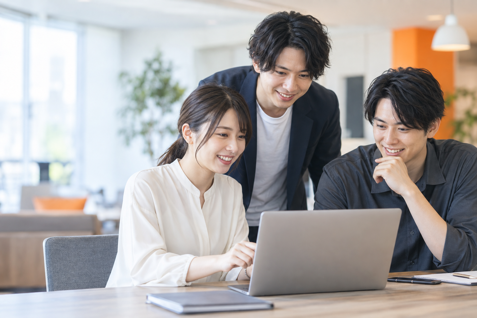 明るいオフィスで、笑顔でパソコンを囲む若いチームのイメージ